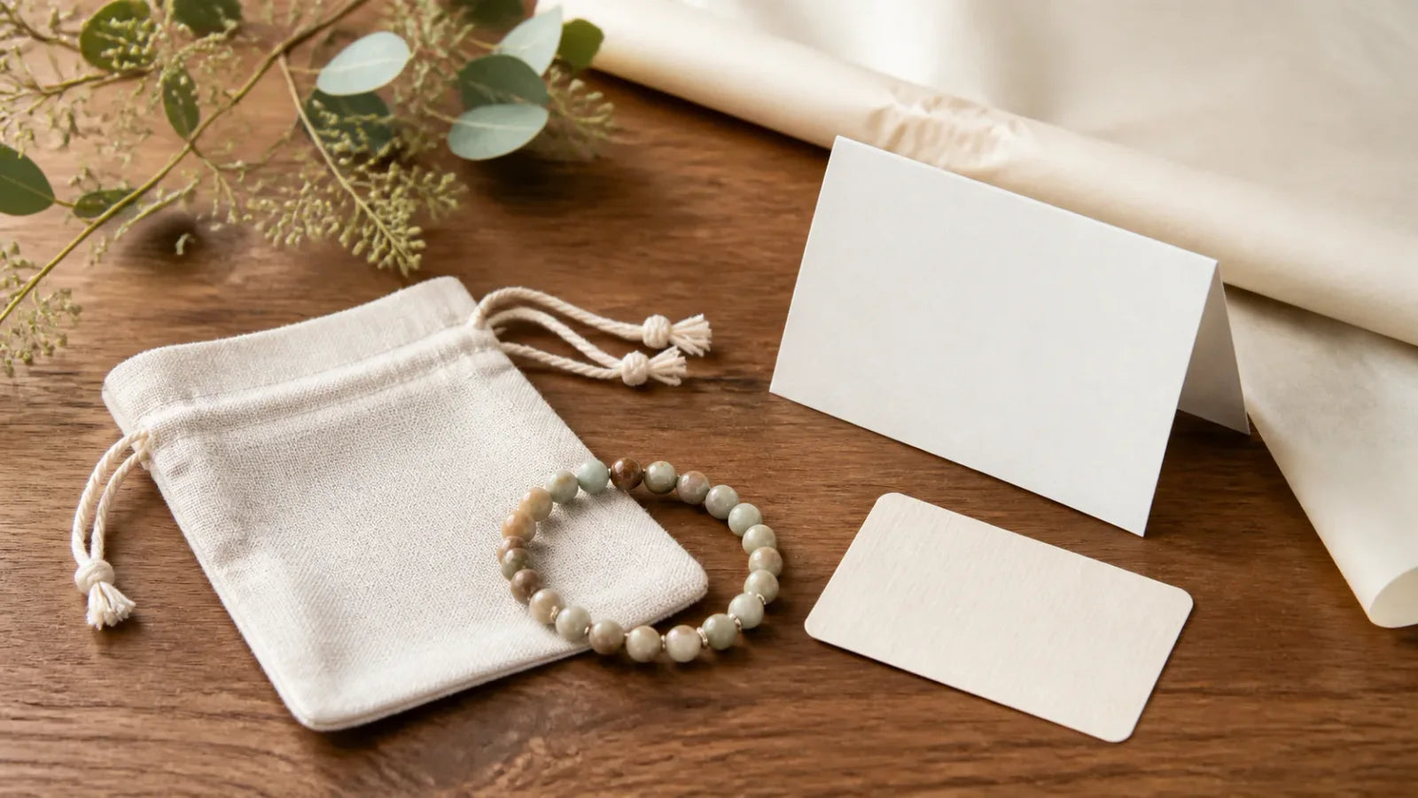 A natural bead bracelet beside a gift message card, care card, and linen pouch